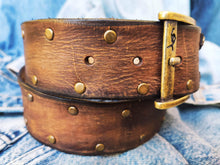 Brown leather belt with two shades of brown two pieces on the front and storage for guitar pick with bronze studs around the belt