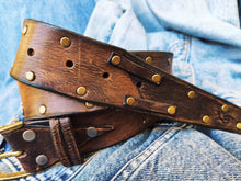 Brown leather belt with two shades of brown two pieces on the front and storage for guitar pick with bronze studs around the belt