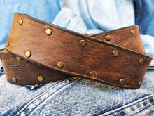 Brown leather belt with two shades of brown two pieces on the front and storage for guitar pick with bronze studs around the belt