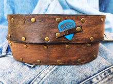 Brown leather belt with two shades of brown two pieces on the front and storage for guitar pick with bronze studs around the belt